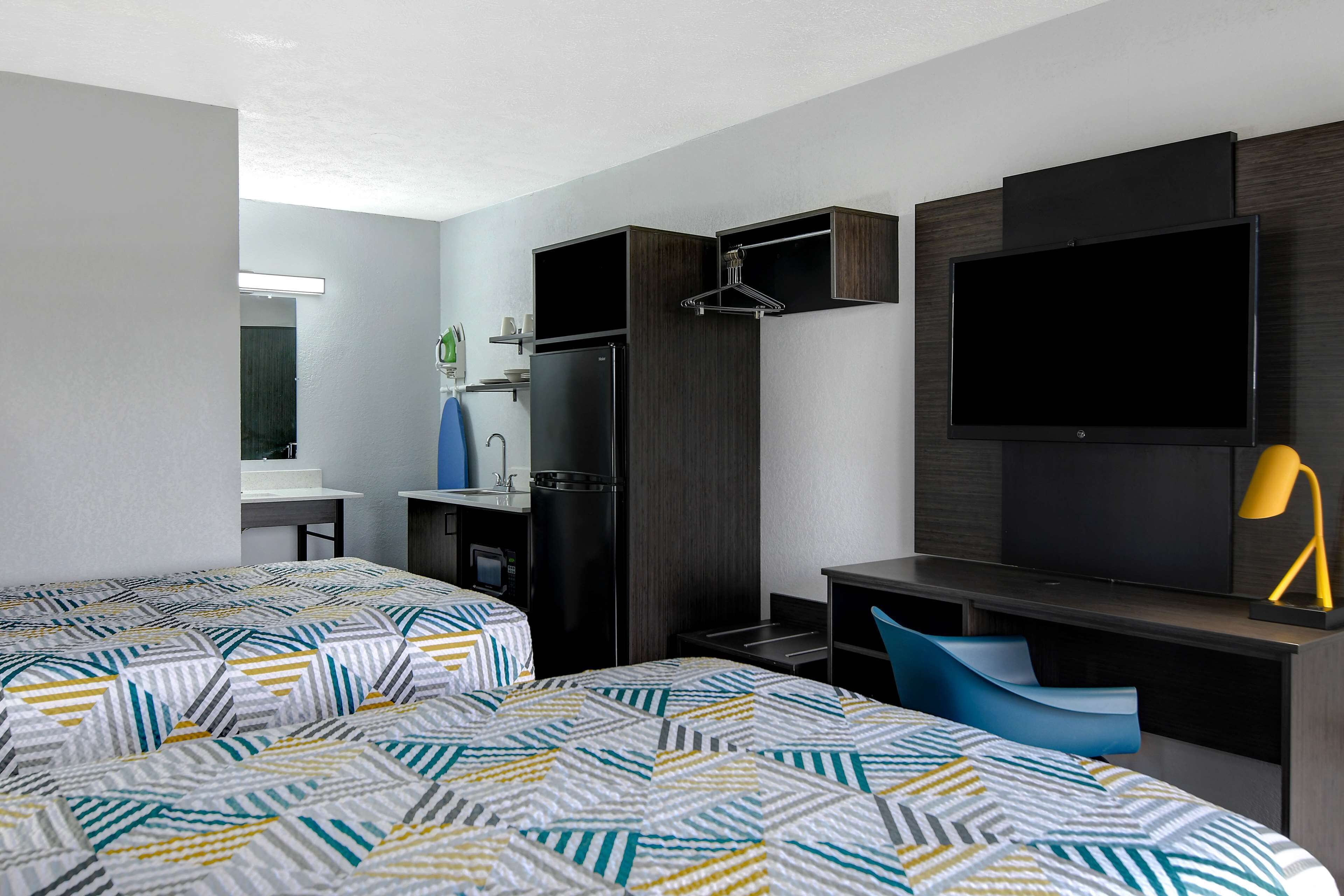 Habitación de hotel con dos camas, un escritorio, un televisor y una kitchenette pequeña.