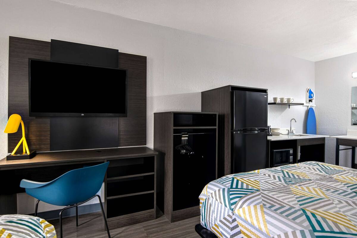 A compact hotel room with a bed, a desk with a chair, a television, a refrigerator, and a microwave.