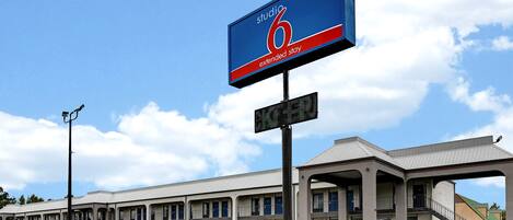 A motel with a large sign reading "Studio 6 Extended Stay." It features a row of rooms with balconies and a central staircase.