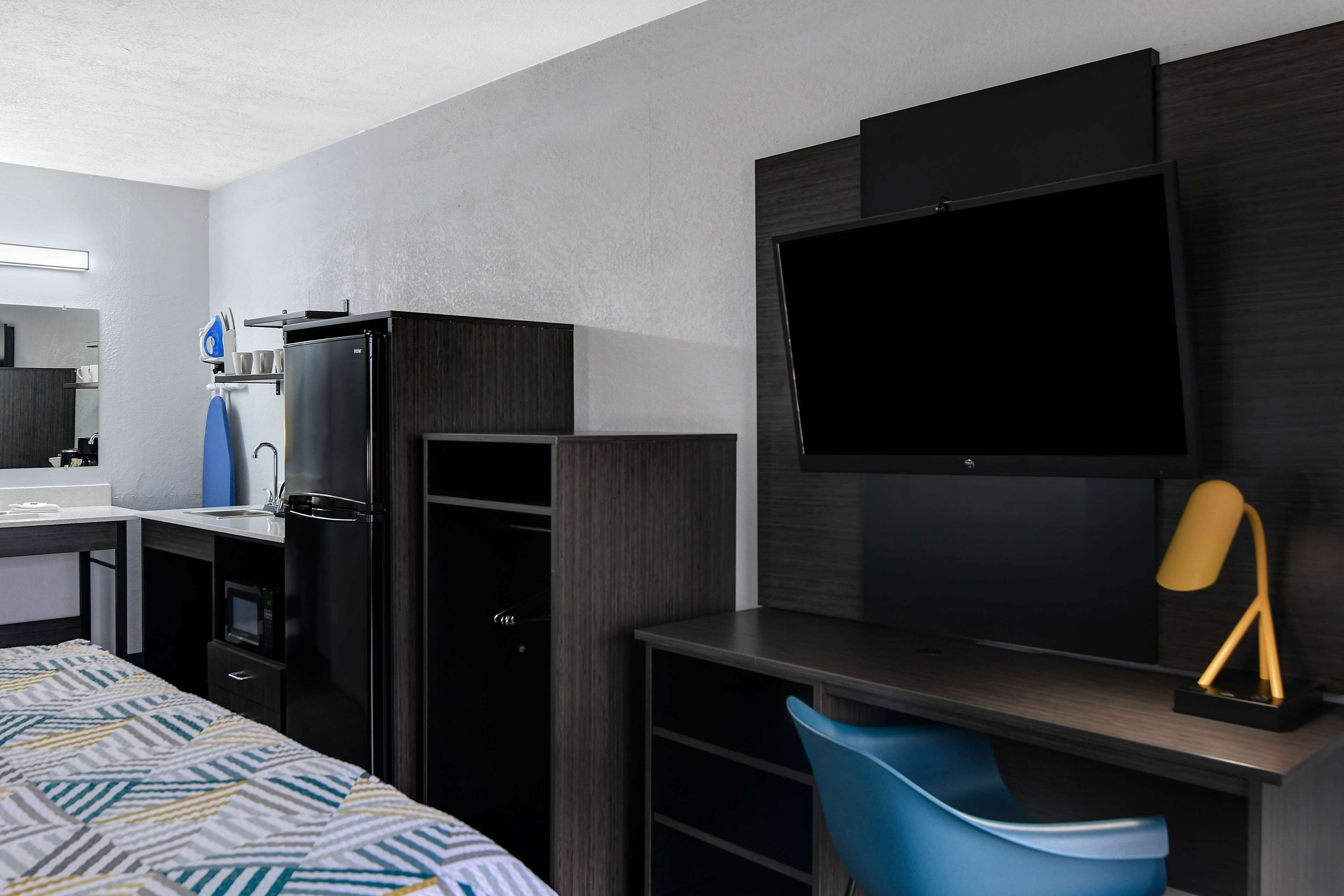 A modern hotel room with a bed, a desk with a chair, a television, a refrigerator, and a microwave.