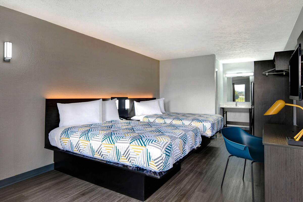 A hotel room with two beds, a desk, a chair, and a TV.