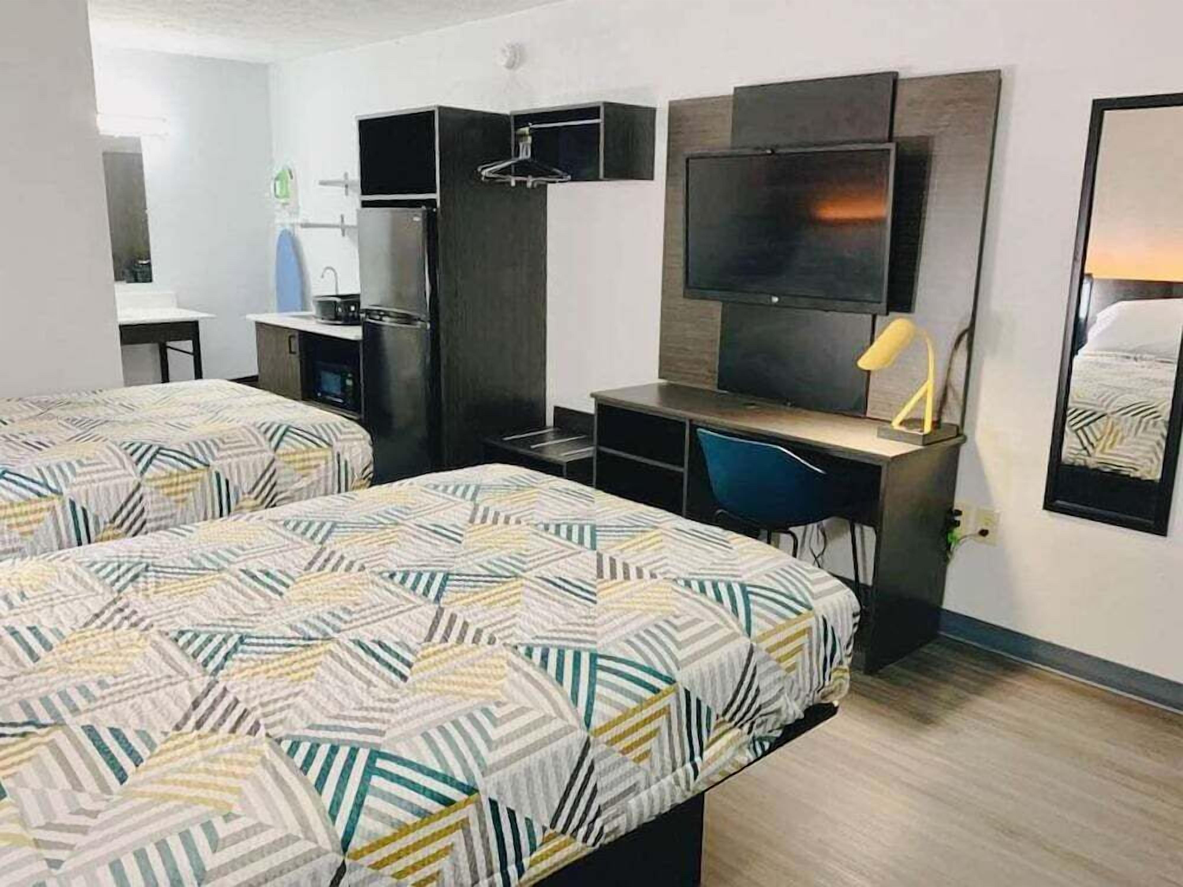 Habitación de hotel con dos camas, un escritorio, un televisor y una kitchenette pequeña.