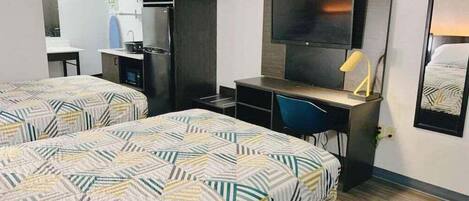 Habitación de hotel con dos camas, un escritorio, un televisor y una kitchenette pequeña.