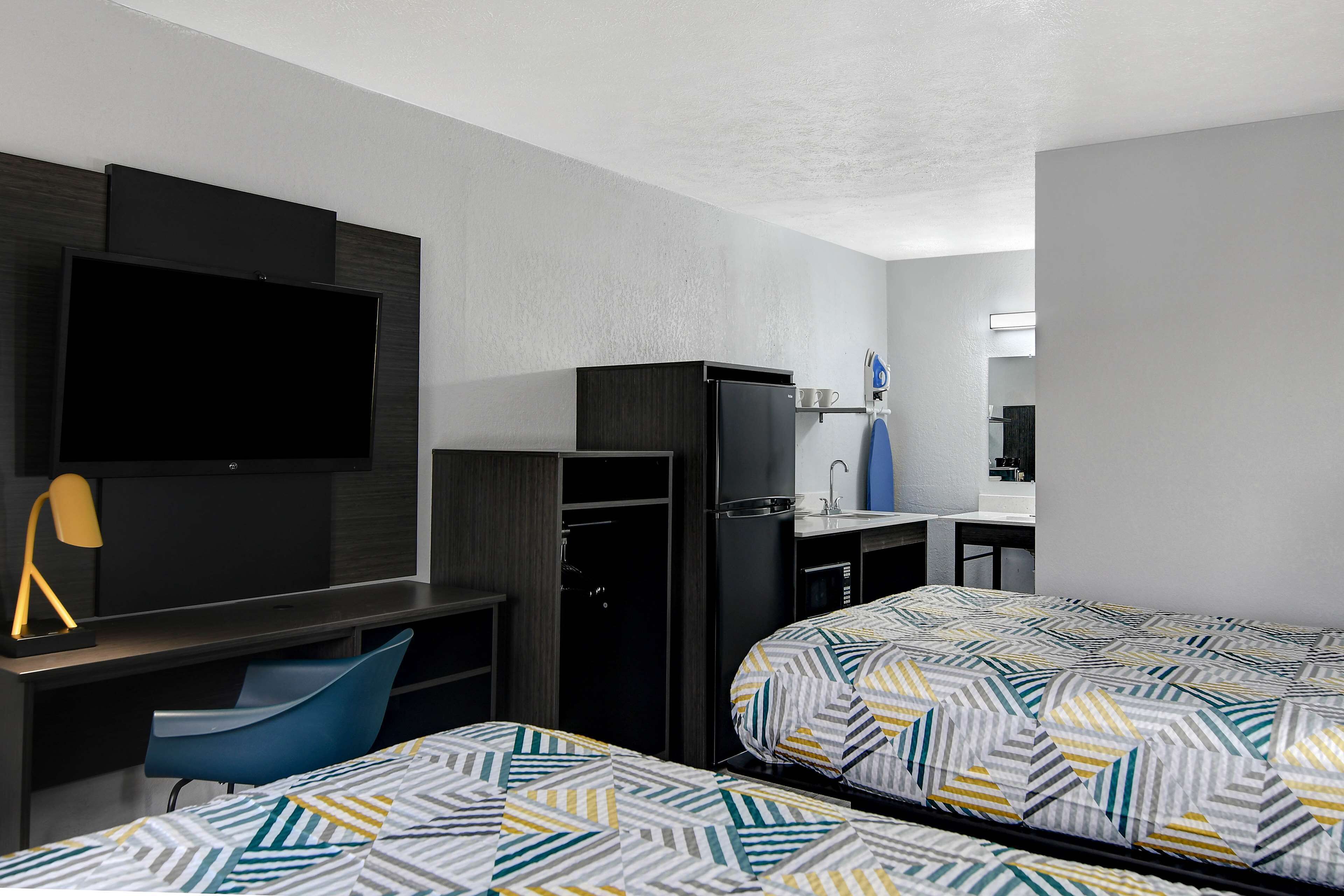 A hotel room with two beds, a desk with a TV, a chair, a wardrobe, and a mirror.