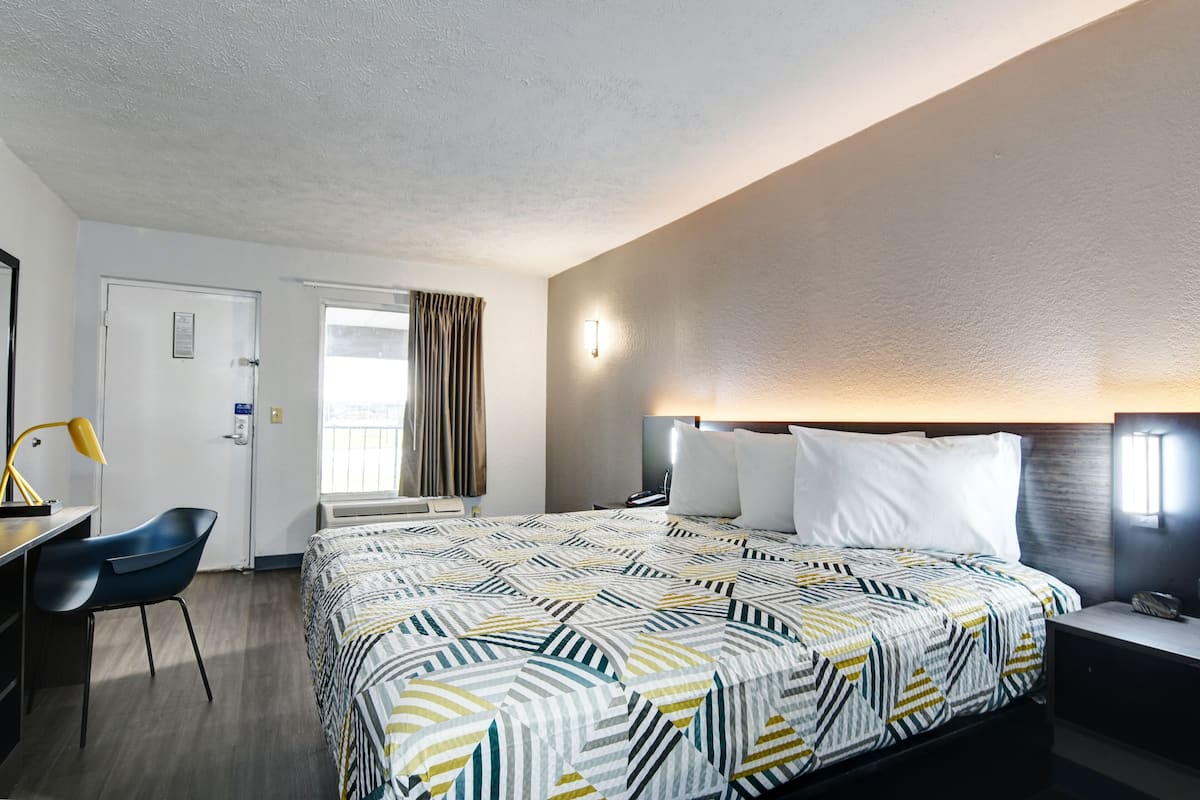 A hotel room with a bed, desk, chair, and a window with curtains.