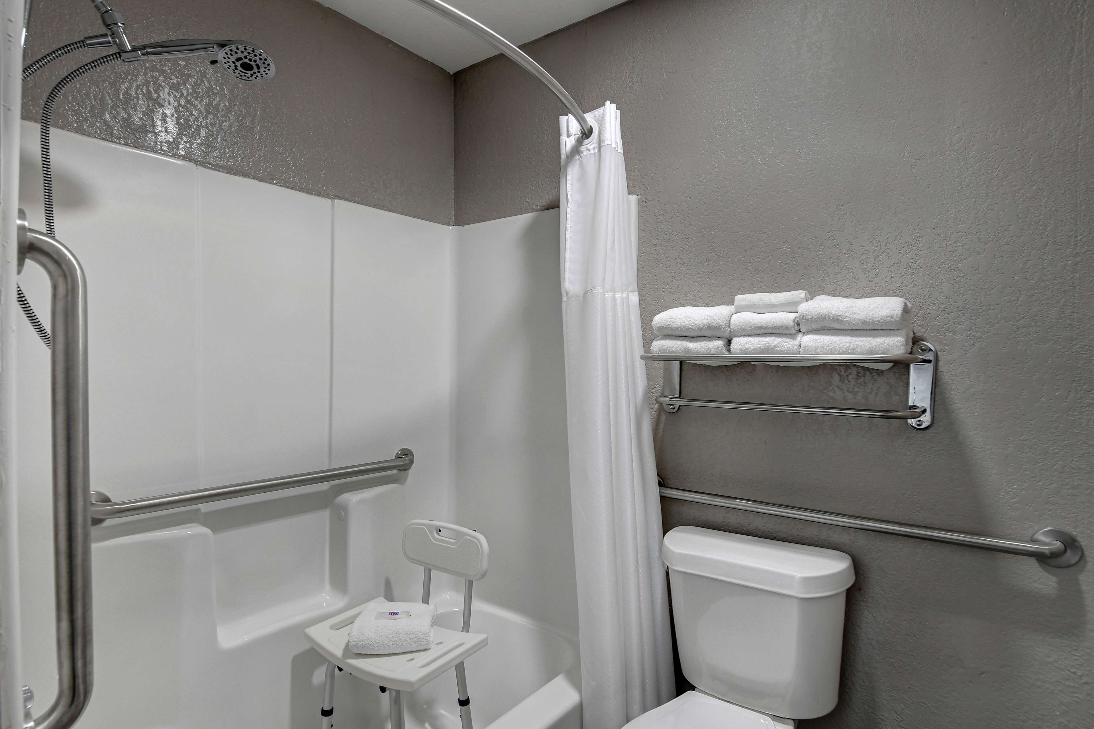 A bathroom with a shower, toilet, grab bars, and a towel rack.