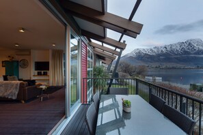 Quarto de hotel moderno com varanda e vista para um lago e montanhas.
