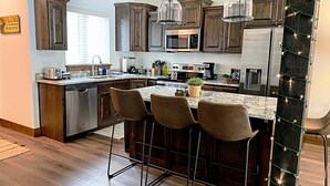 Una cucina moderna con mobili in legno scuro, elettrodomestici in acciaio inossidabile, un'isola in marmo con sgabelli da bar e illuminazione a sospensione.