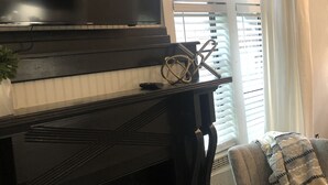 Ett vardagsrum med ett svart piano, en platt-TV och ett fönster med persienner.