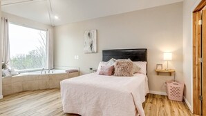 A bedroom with a bed, a bedside table, a window seat, and a view of the outdoors. - Enchanting Memory Maker-Treetop Hideaway-Jacuzzi (Stigler)