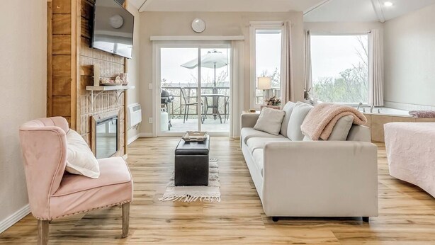 A spacious living area with a fireplace, a sofa, a coffee table, and a television mounted on a wooden wall. - Enchanting Memory Maker-Treetop Hideaway-Jacuzzi (Stigler)