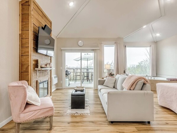 A spacious living area with a fireplace, a sofa, a coffee table, and a television mounted on a wooden wall. - Enchanting Memory Maker-Treetop Hideaway-Jacuzzi (Stigler)