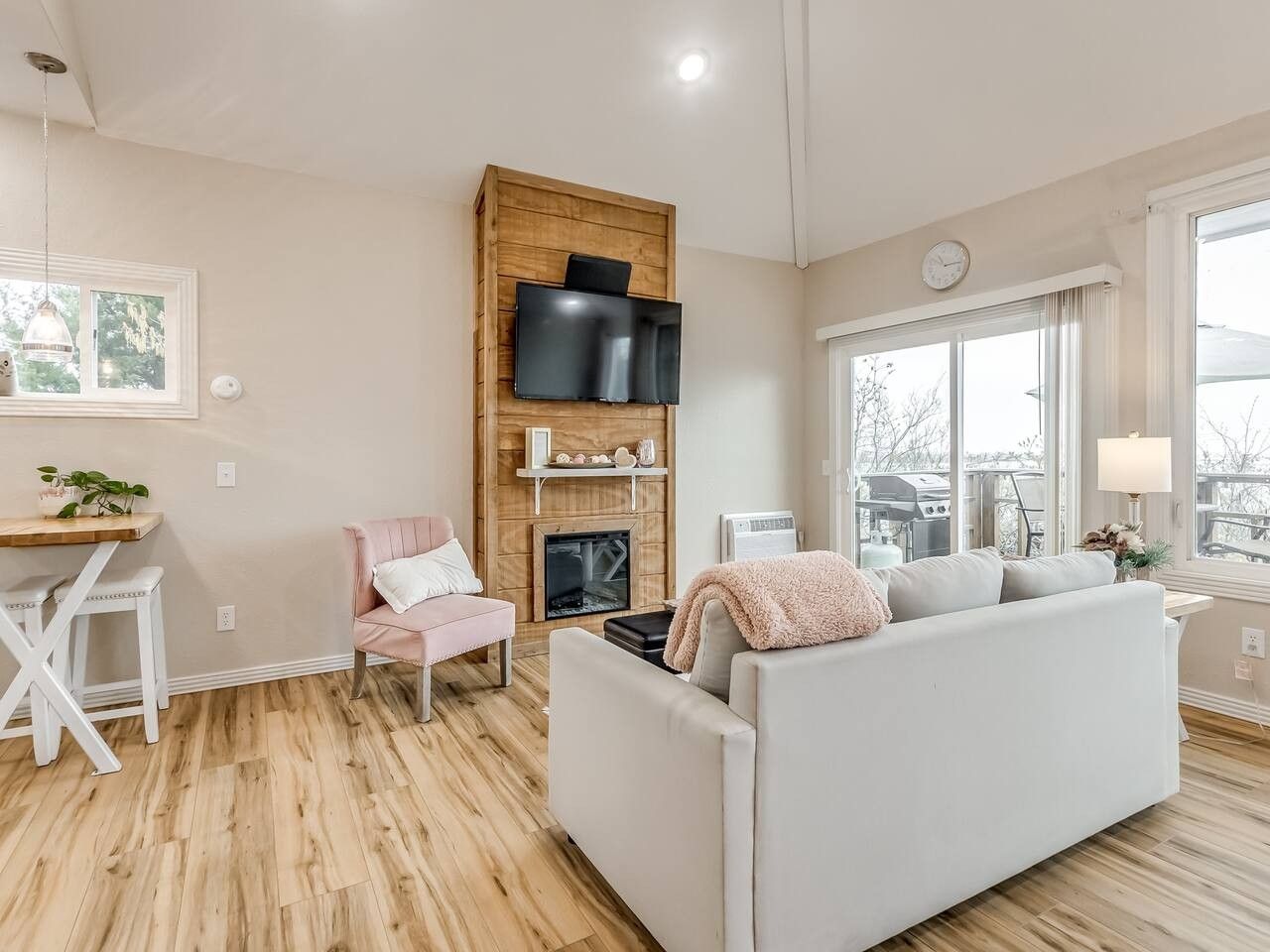 Een moderne woonkamer met een bank, een roze fauteuil, een houten tv-meubel en een open haard.