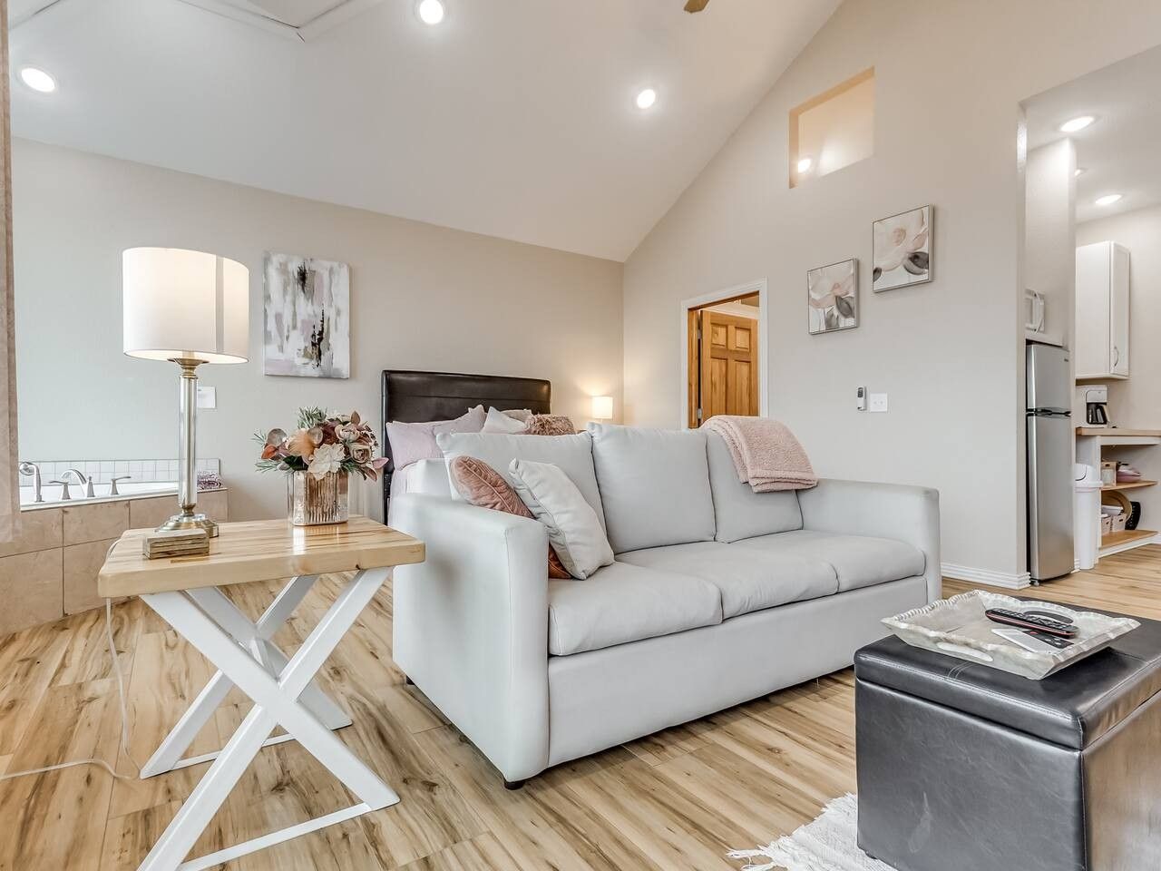 A modern living room with a white sofa, a coffee table, a dining table with a lamp, and a kitchen area in the background.