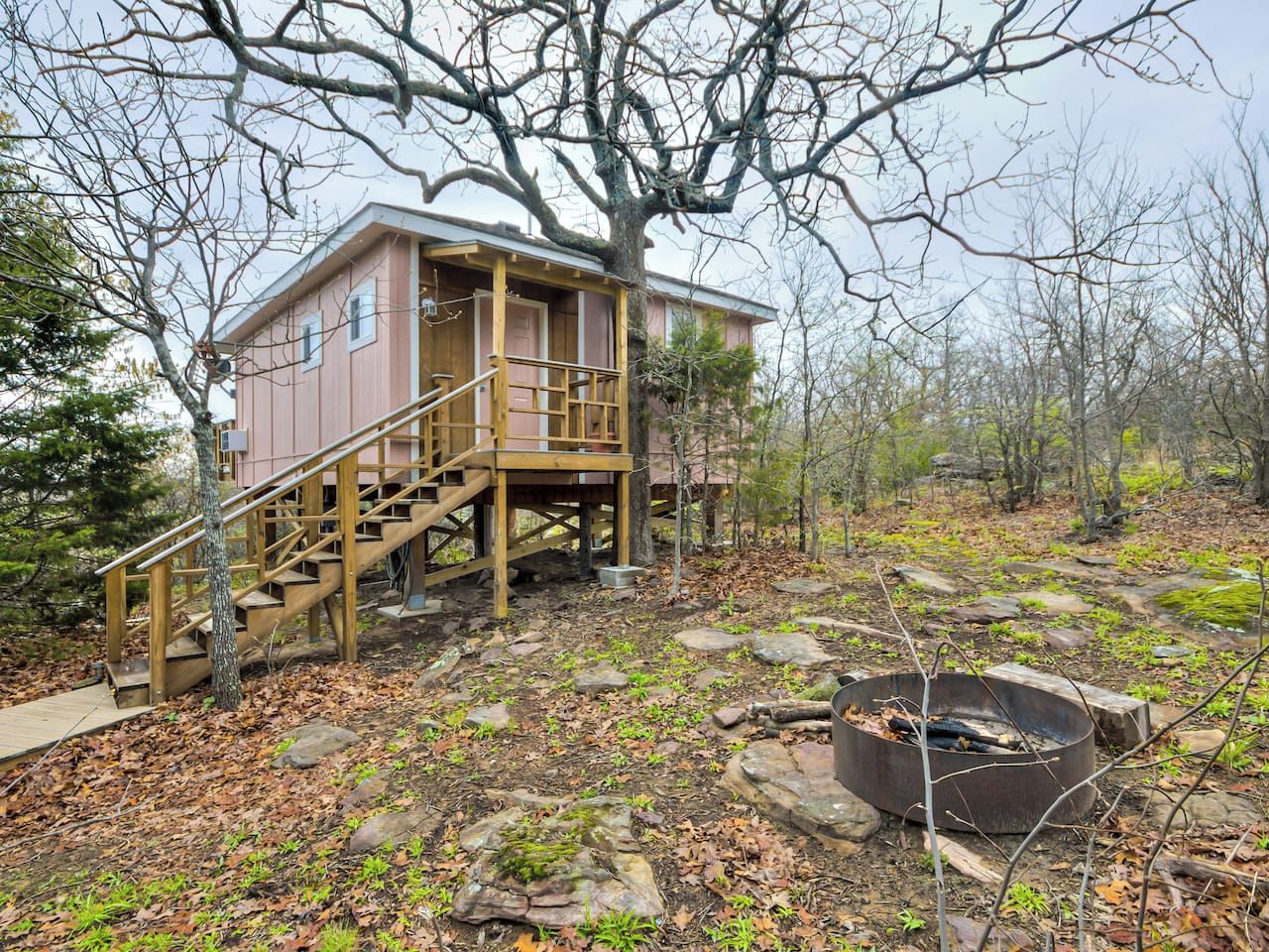 A cabin with a wooden staircase and a fire pit in the yard.