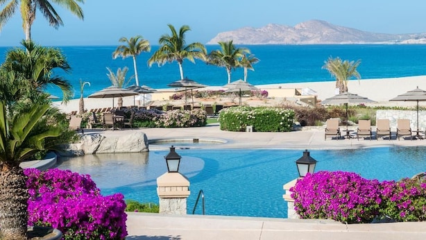 A resort pool area with palm trees, lounge chairs, and a view of the sea. - Beachfront Golf & Spa Paradise at Casa Del Mar (San Jose del Cabo)