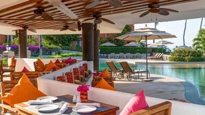 A poolside dining area with tables set for two, lounge chairs, and umbrellas. - Beachfront Golf & Spa Paradise at Casa Del Mar (San Jose del Cabo)