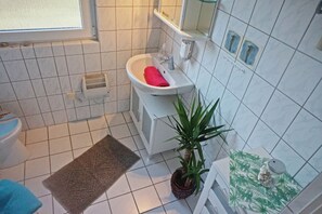 A bathroom with a white sink, a red towel, a potted plant, and a patterned rug.