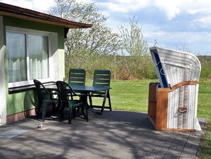 A patio with a table and chairs, a wicker chair, and a building with a green exterior and a window.