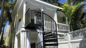 Un bâtiment à deux étages, à l’extérieur blanc, doté d’un escalier en colimaçon noir et d’un balcon avec des balustrades blanches.
