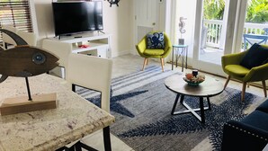 Un salon avec un téléviseur, une table en bois en forme de poisson, un fauteuil jaune et un canapé bleu.
