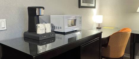 A hotel room with a kitchenette, a microwave, a coffee maker, and a framed picture on the wall.