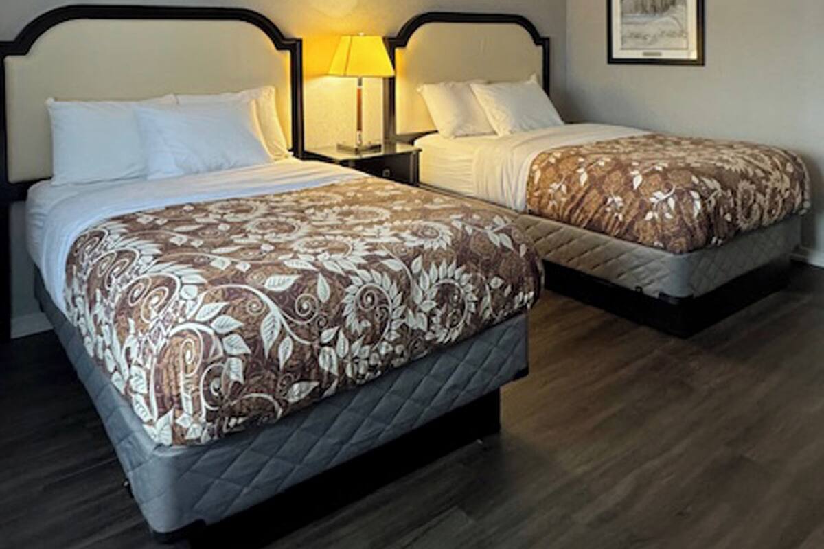 Quarto de hotel com duas camas, cada uma com colcha estampada, luminárias laterais e um quadro na parede.