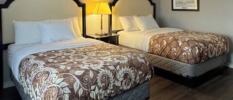 A hotel room with two beds, each with a patterned bedspread, bedside lamps, and a framed picture on the wall.