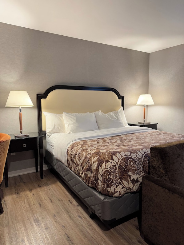Habitación de hotel con una cama, dos mesitas de noche con lámparas, una silla y suelo de madera.