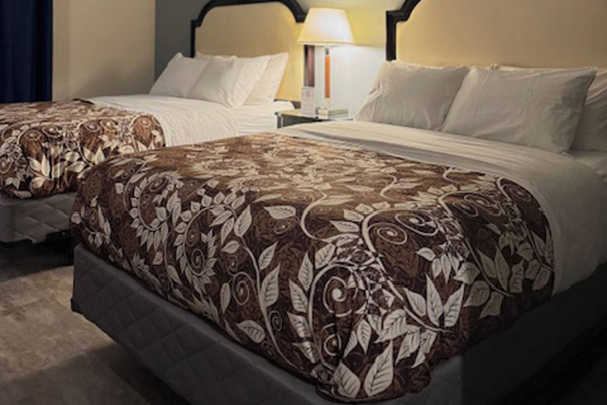 Quarto de hotel com duas camas, cada uma com colcha estampada, mesa de cabeceira e abajur.