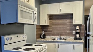 A modern kitchen with white cabinets, a built-in microwave, a stove, and a coffee maker. - Big Bird Inn Wawa, SureStay Collection by Best Western (Wawa)