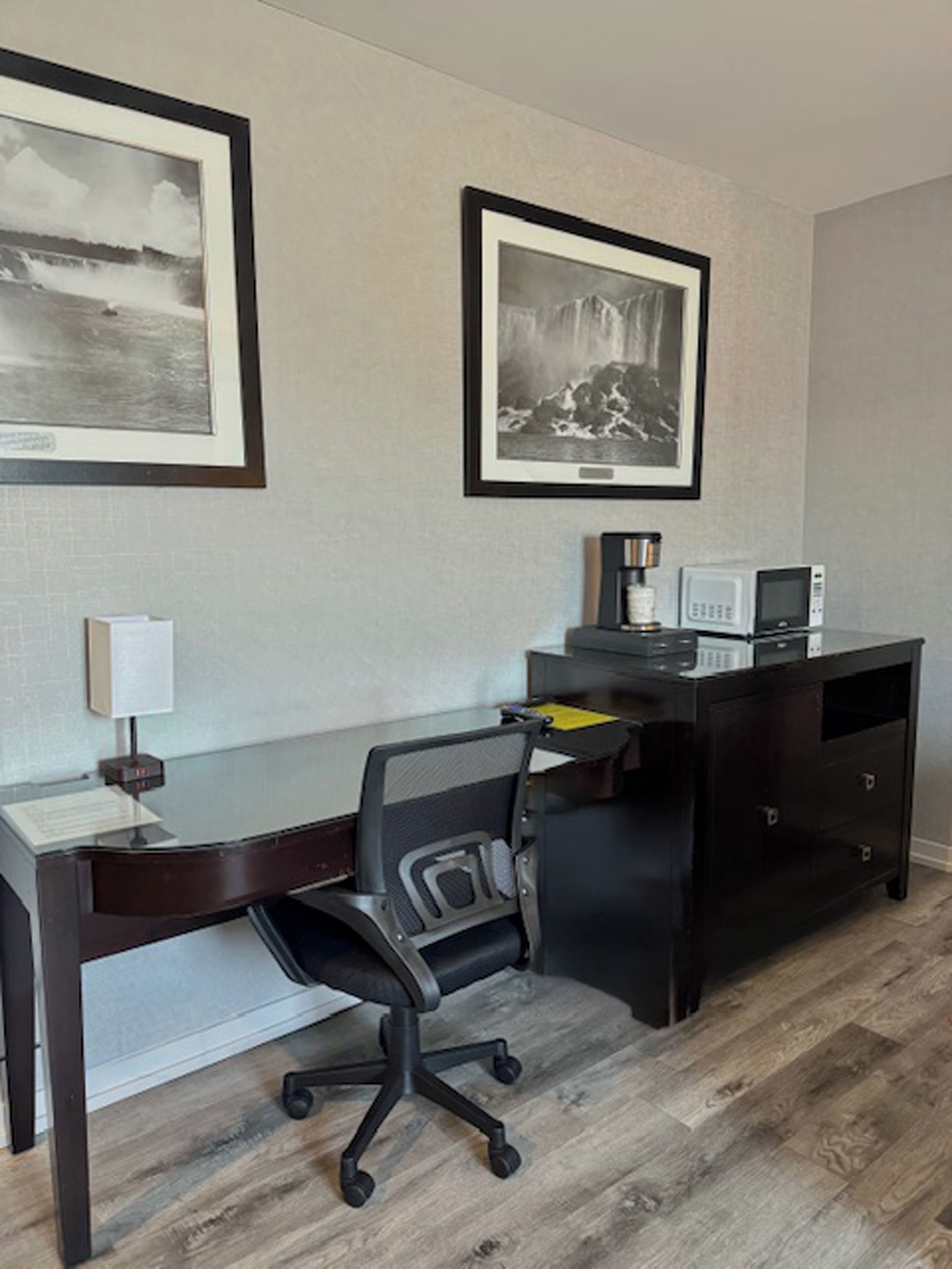 Une chambre d’hôtel équipée d’un bureau, d’une chaise et de deux tableaux encadrés accrochés au mur.
