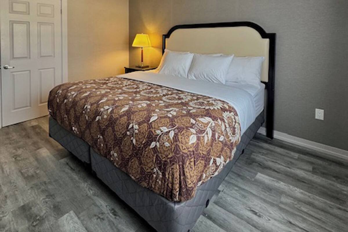 Um quarto com uma cama, uma mesa de cabeceira, uma luminária e uma porta.