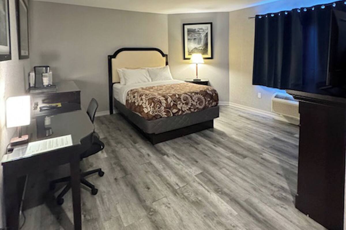 Quarto de hotel com cama, mesa, cadeira, televisão e abajur.