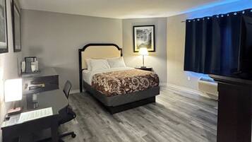 Una habitación de hotel con cama, escritorio, silla, televisión y lámpara.