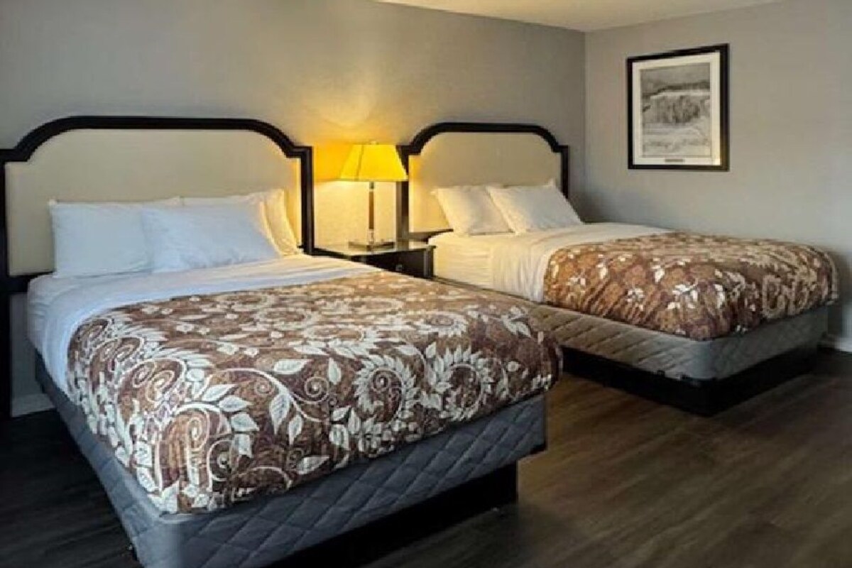A hotel room with two beds, each with a headboard, a bedside table, and a lamp.