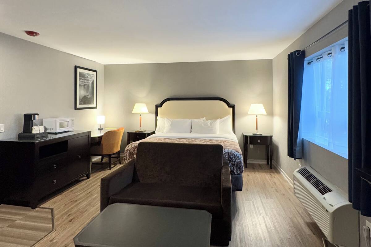 Quarto de hotel com cama, escrivaninha, cadeira, máquina de café, televisão e ar condicionado.