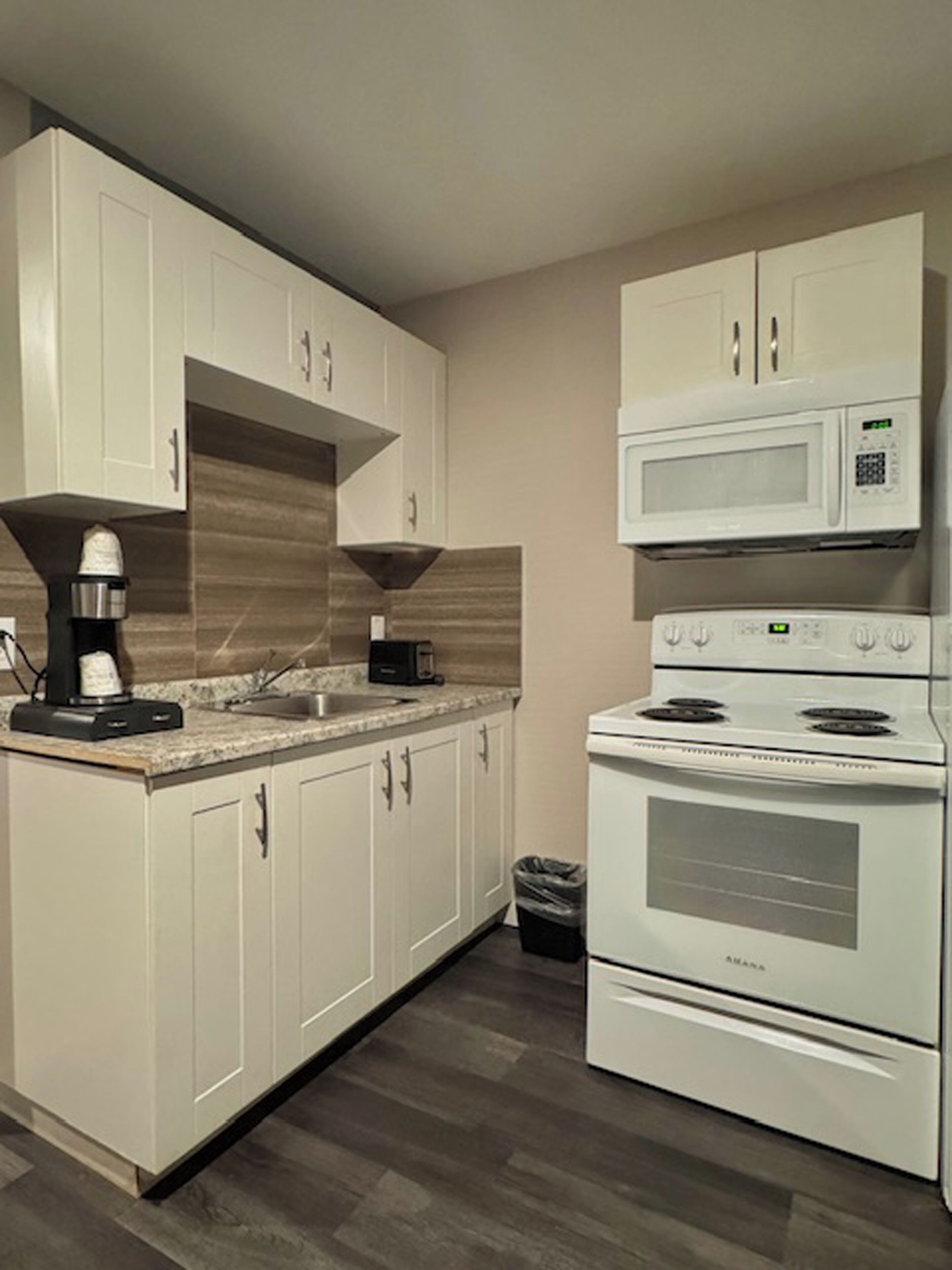 A modern kitchen with white cabinets, a built-in microwave, a stove, and a coffee maker.