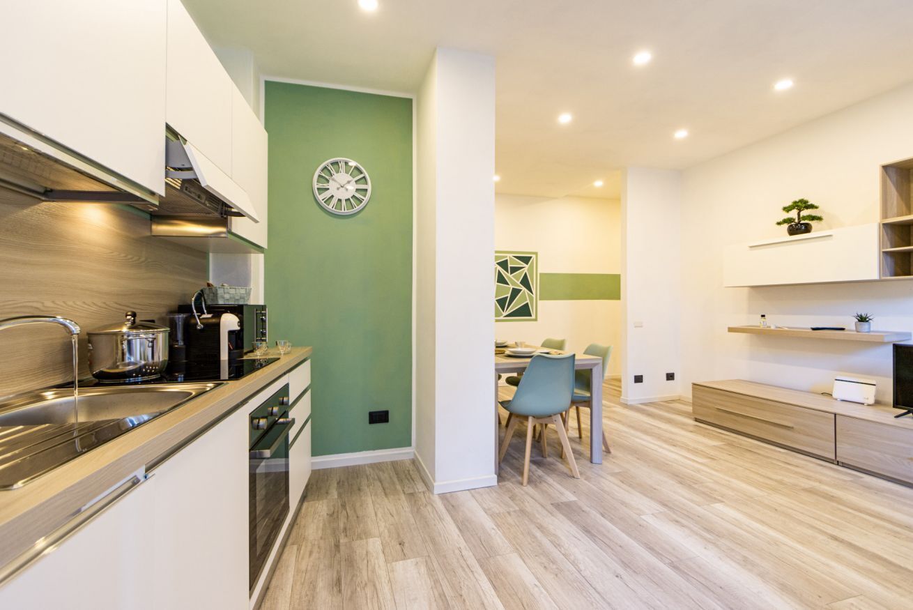 Una cocina moderna con una pared de acento verde, un reloj y una zona de comedor con sillas y una mesa.