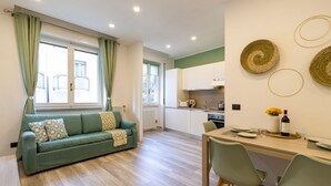 A modern living room with a sofa, dining table, and kitchen area. - Green Pearl ☆☆☆☆☆ - Apartment 100 meters from the lake - WiFi - By Guestaly (Arona)