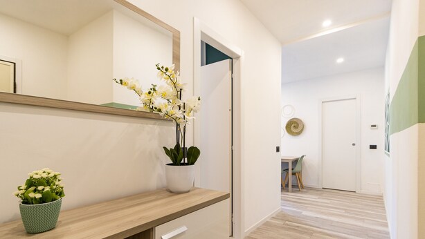 A modern hotel hallway with a wooden reception desk, a potted plant, a mirror, and a door leading to a room. - Green Pearl ☆☆☆☆☆ - Apartment 100 meters from the lake - WiFi - By Guestaly (Arona)