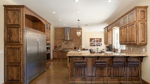 A spacious kitchen with wooden cabinetry, a stainless steel refrigerator, and a central island with bar stools.