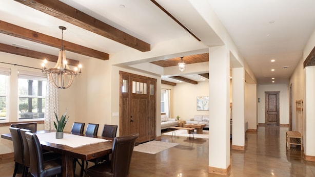A spacious dining area with a wooden table and chairs, a chandelier, and a large wooden door.