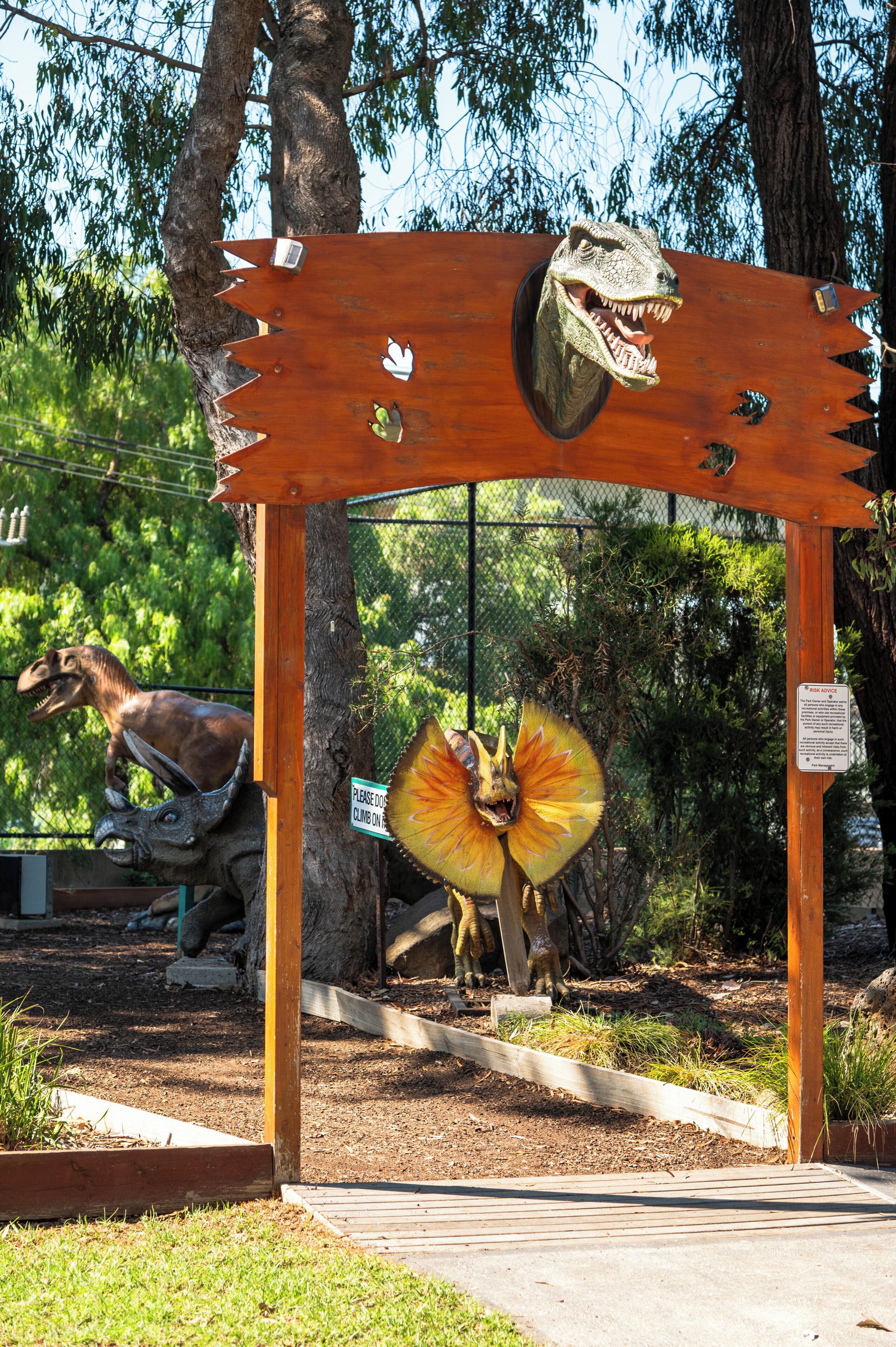 Une exposition sur les dinosaures, avec une arche en bois et un panneau invitant les visiteurs à grimper dessus.