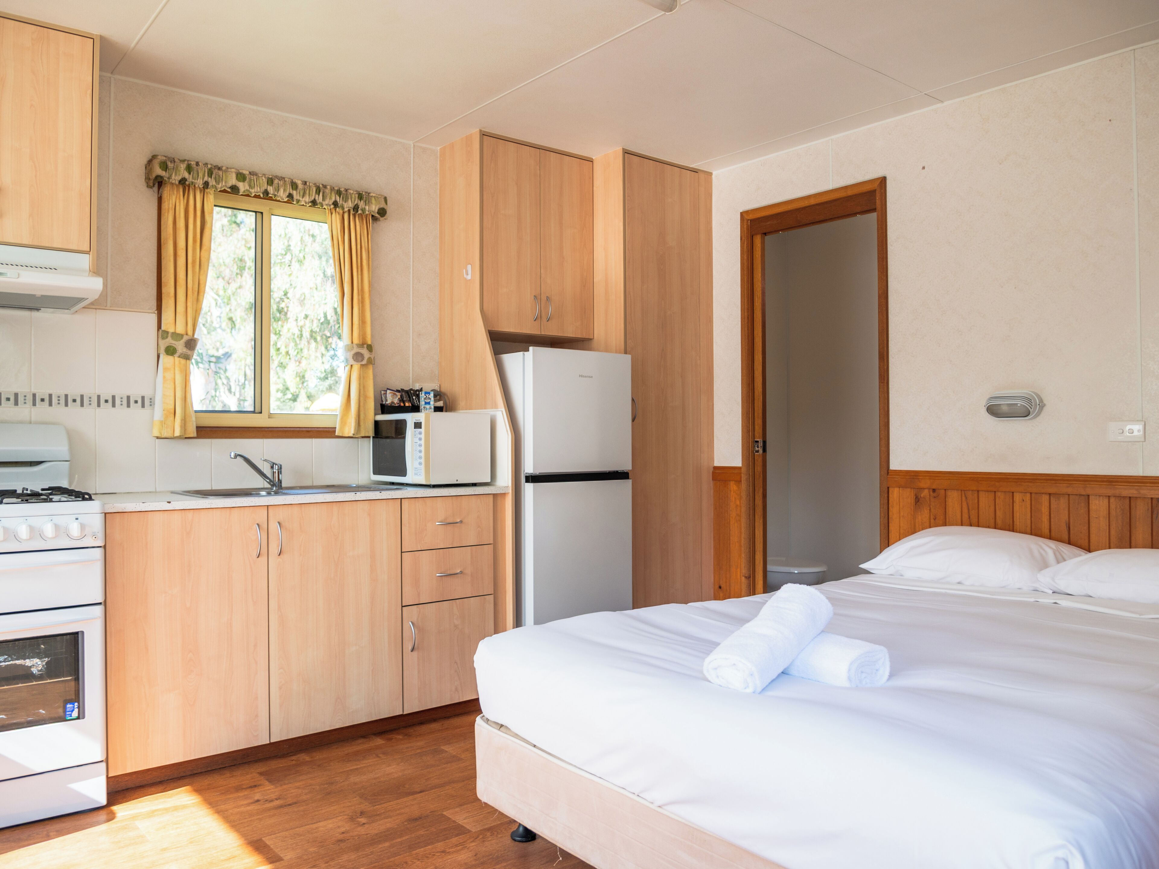 A compact room with a bed, a kitchenette with a microwave, a refrigerator, and a stove.