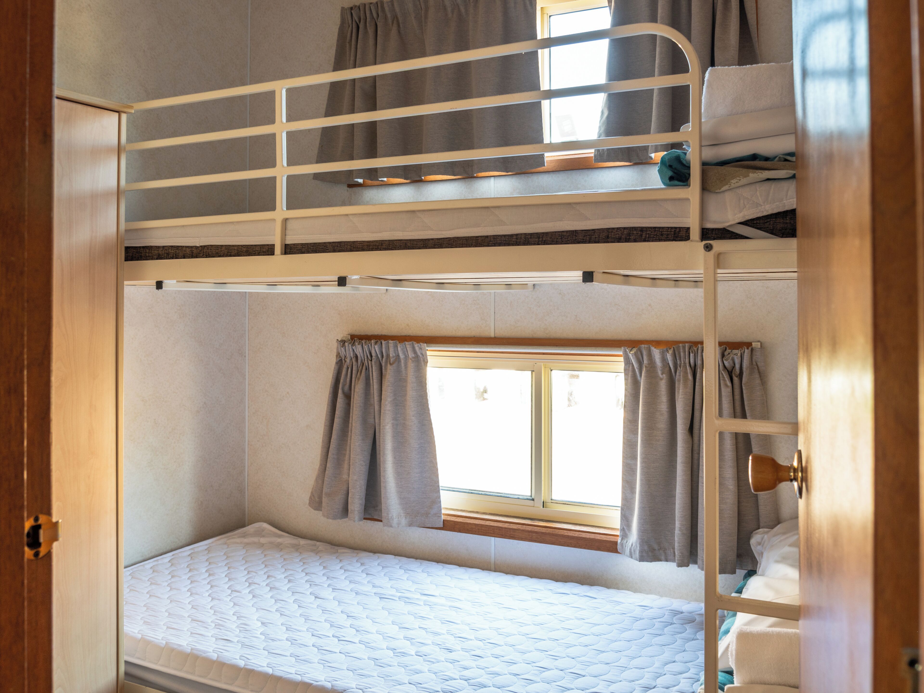 A bunk bed room with a window, curtains, and a door.