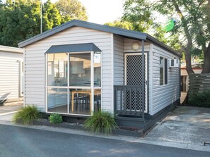 A single-story mobile home with a front porch, a small deck, and a window overlooking the street. - Geelong Holiday Park (Belmont)