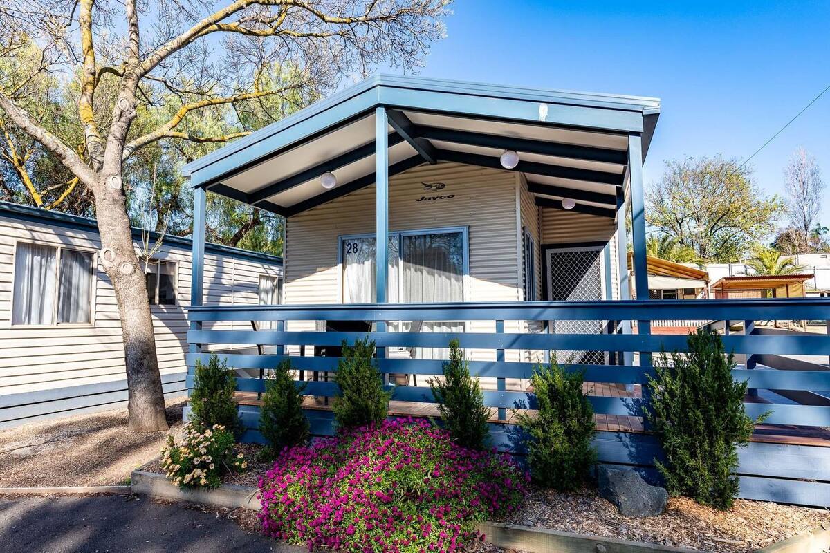 A mobile home with a covered porch, number 28, and a small garden with pink flowers.