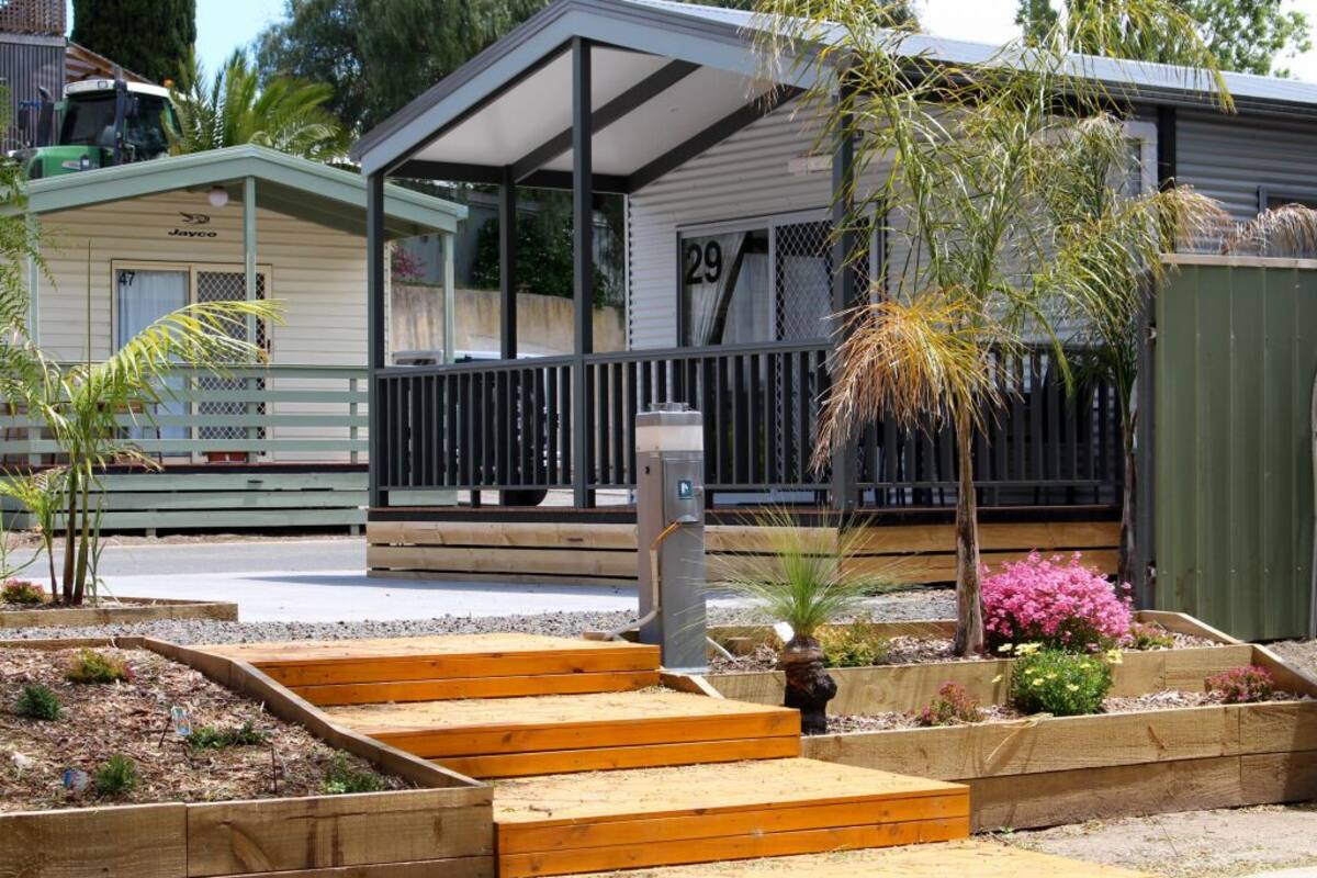 A mobile home with a porch, wooden steps, and a garden with various plants.