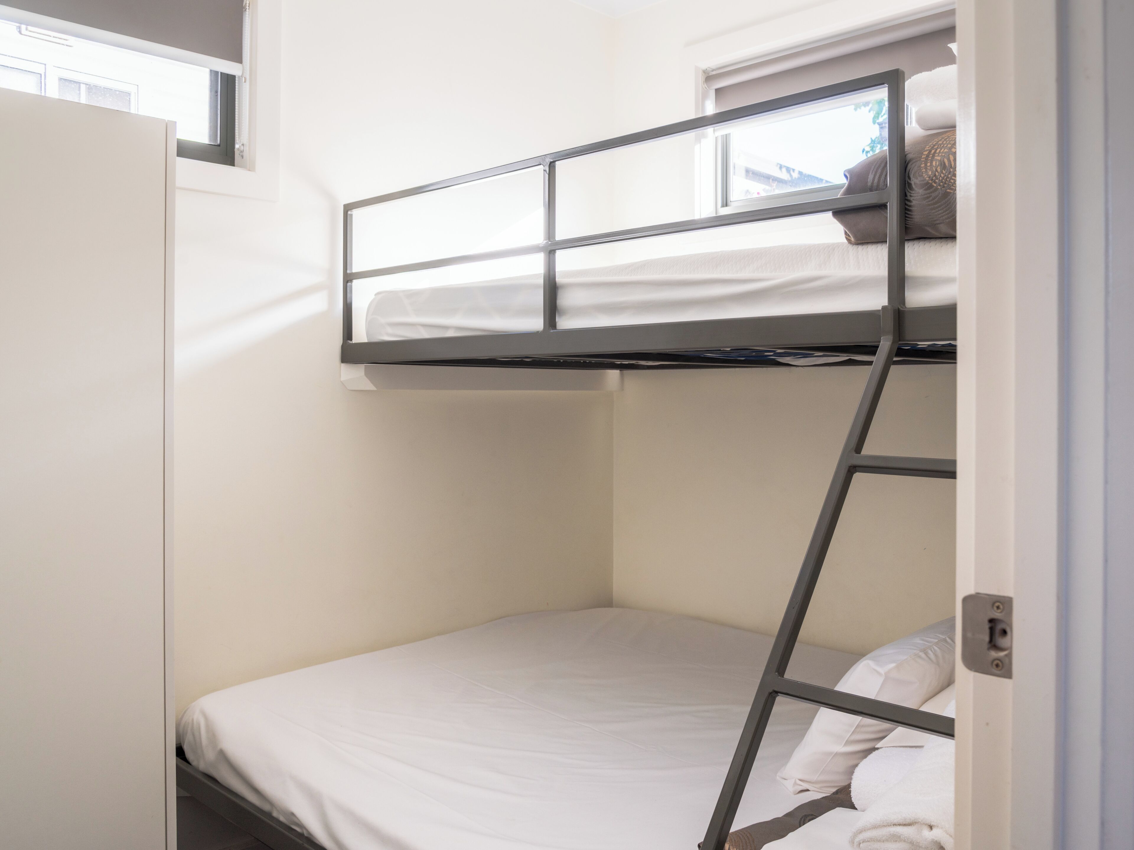 A bunk bed with a ladder, a window, and a door.
